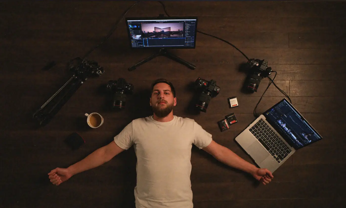 Matt lying on a wooden floor surrounded by cameras, a monitor and a laptop